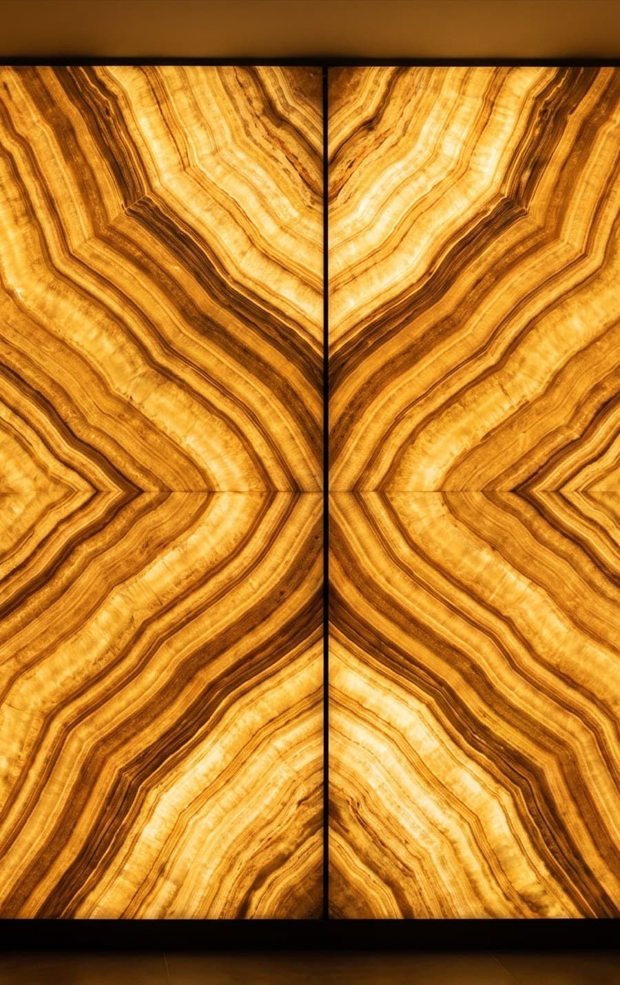 A book-matched backlit onyx wall, two mirrored slabs glowing amber from within