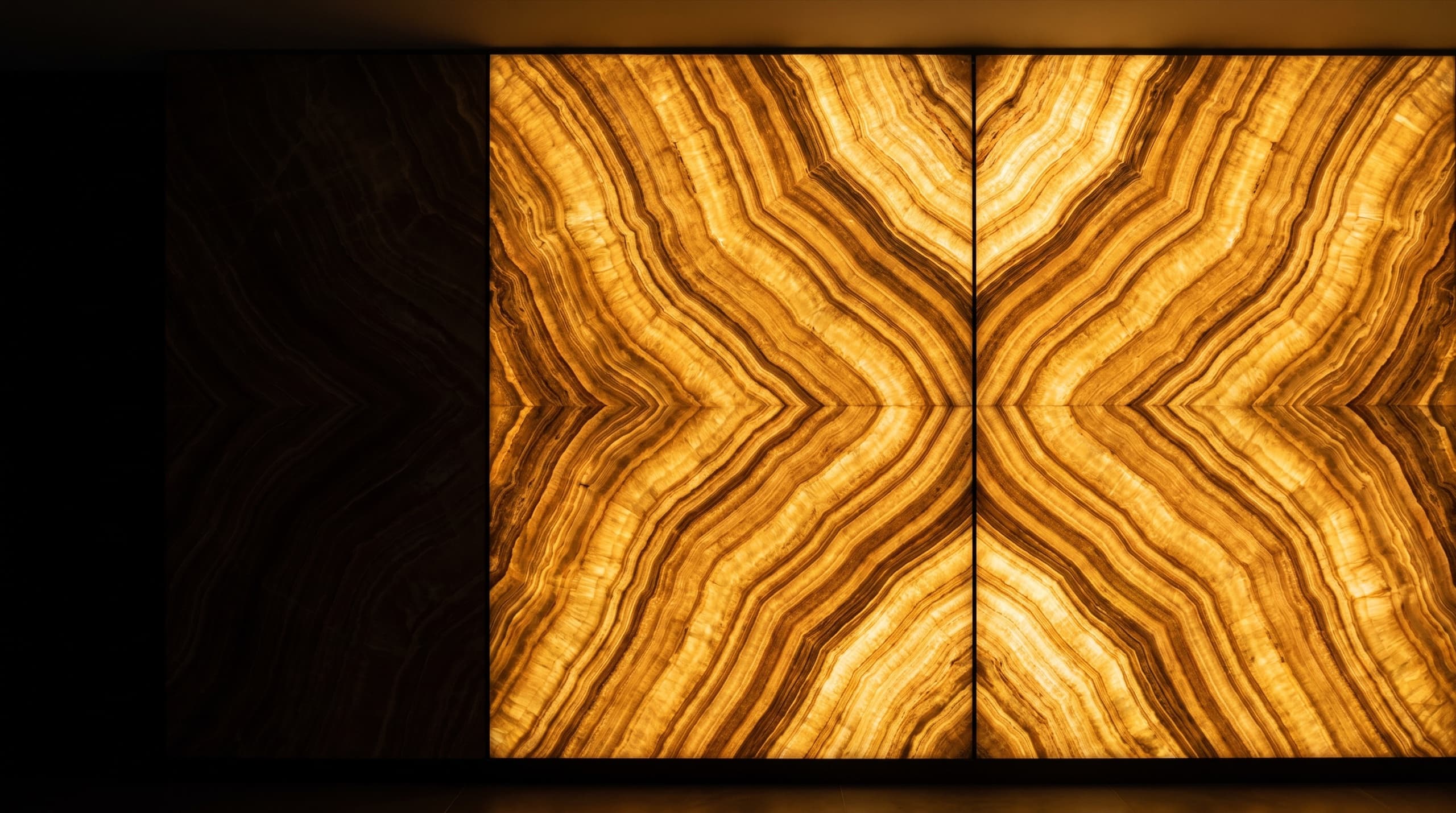 A book-matched backlit onyx wall, two mirrored slabs glowing amber from within